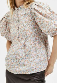 Blusa floreale in tessuto leggero con maniche a palloncino, chiusura a bottoni e vita arricciata. Colori pastello con motivo floreale.