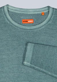 Hellgrüner Pullover mit strukturiertem Strick, rundem Ausschnitt und orangefarbenem Markenschild. Mit gerippten Bündchen an Ärmeln und Saum. Größenschild ist sichtbar.