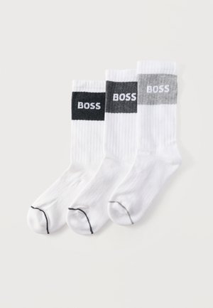 Trois chaussettes montantes blanches avec une texture côtelée et des bandes noire, gris foncé et gris clair en haut, chacune portant l'inscription "BOSS" en blanc.