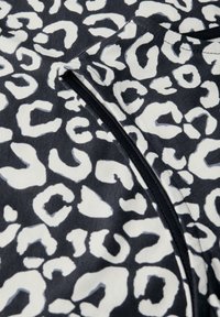 Tessuto nero con un motivo a stampa di leopardo bianco, con una texture liscia e un dettaglio di cucitura visibile nel design.