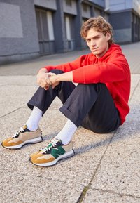 Kengät, joissa on sekoitus beigeä, vihreää ja ruskeaa, joissa on teksturoitu mokkanahkainen päällinen, nauhat ja musta kumipohja. Yhdistetty valkoisten sukkien kanssa.