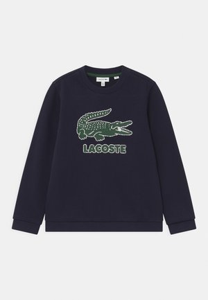 Marine sweatshirts lavet af bomuld. Har et stort grønt krokodille-logo med en prikket tekstur og "LACOSTE"-tekst under. Standard rund hals.