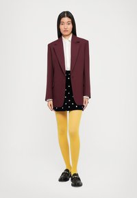 Burgundy oversized blazer over a white lace blouse, paired with a black skirt featuring silver embellishments and yellow tights. Black loafers.