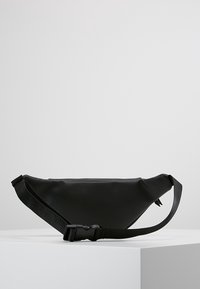 Musta vyölaukku, joka on valmistettu sileästä synteettisestä materiaalista, kolmion muotoinen, säädettävä olkahihna ja sivulla oleva solki.