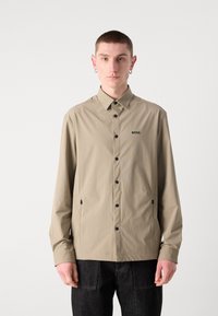 Camicia button-up beige chiaro con colletto, dotata di bottoni neri e un piccolo logo nero "BOSS". Realizzata in un tessuto liscio e textured.