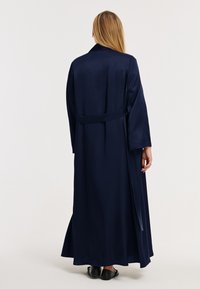 Robe longue en satin bleu marine avec une taille ceinturée et de larges manches, présentant une texture lisse et une coupe longueur cheville.