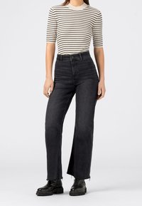 Černé džíny s vysokým pasem a rovnými nohavicemi, s ošlehanými lemy a hladkou džínovou texturou, doplněné pruhovaným krátkým rukávem.