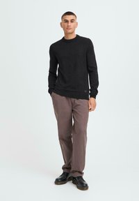 Black knit sweater with round neckline, long sleeves, and ribbed hem, paired with light brown pants and black footwear. Simple design, neutral colors.