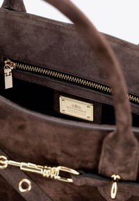 Interno di una borsa in suede marrone con una cerniera dorata, accessori in oro, etichetta in pelle con la scritta "WITTCHEN HANDMADE IN ITALY" e superficie texturizzata.