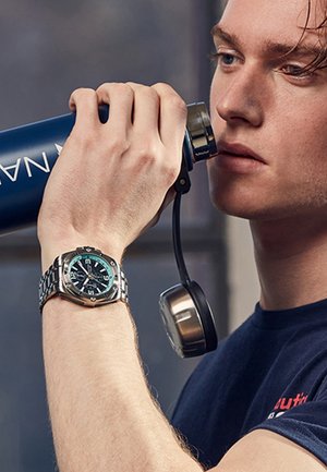 Montre en acier inoxydable argenté avec un cadran bleu foncé, index des heures argentés, et un bracelet en métal ; personne tenant une bouteille d'eau bleue avec un capuchon argenté.