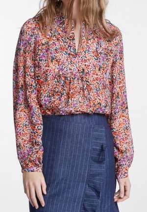 Langærmet blomstrede bluse i orange, pink og lilla nuancer kombineret med en blå, stribet nederdel med flæsedetalje.