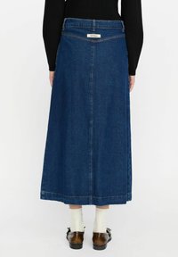 Denim maksi suknja u tamnoplavoj boji s ravnim krojem, s oznakom straga. Glatka tekstura i dizajn do gležnjeva, vidljive detaljne šavove.
