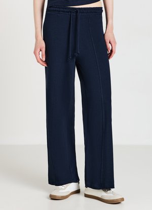 Pantaloni a gamba larga blu navy realizzati in tessuto morbido, dotati di una vita elastica con cordoncino e cuciture laterali, abbinati a sneaker bianche casual.