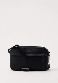 Črna torba za čez ramo z gladko teksturo, ki ima na sprednji strani logotip, nastavljiv trak in predale z zadrgo.