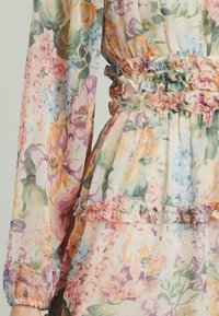 Blumenmuster-Kleid aus leichtem Stoff, mit sanften Farbtönen, Rüschendetails an Taille und Ärmeln sowie einer taillierten Silhouette.