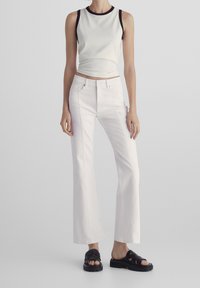 Witte uitlopende jeans met voornaad, gecombineerd met een lichte tanktop met zwarte rand. De schoenen zijn zwart, chunky en gevlochten.