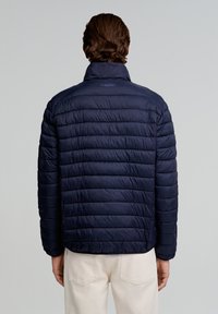Chaqueta acolchada navy con cuello alto, diseño acolchado, textura ligera y logo bordado "SCALPERS" en la parte trasera.