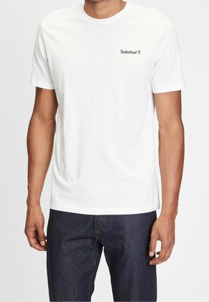 Valkoinen puuvillapaita, jossa on pyöreä kaula-aukko ja lyhyet hihat, sekä pieni musta Timberland-logo vasemmassa ylärintapielessä.