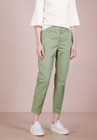 Chinos verde chiaro con un design aderente, realizzati in cotone. Presentano una chiusura con bottone, tasche laterali e gambe affusolate. Abbinati a sneaker bianche.