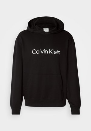 Melna kokvilnas kapuce ar priekšējo kabatu, kurai ir balts "Calvin Klein" logo uz krūtīm un ribotas aproces un apakšmala.