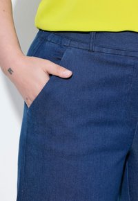 Mörkblå denimbyxor med en slät yta, med en sidoficka. Kombinerat med en ljusgul topp som delvis är synlig ovanför midjan.