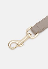 Šedý faux kožený řemínek se zlatým kovovým zapínáním; má texturovaný povrch a švy jako akcenty. Zapínání obsahuje rytí značky.