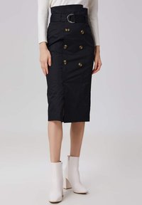 Jupes noire en crêpe avec une taille haute, boutons dorés à double boutonnage, ceinture avec une boucle circulaire et une fente avant ; associée à des bottines blanches.