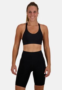 Svart sport-bh med texturerad yta och breda band, tillsammans med h�ögmidjade svarta shorts med en slät tyg och plana sömmar.