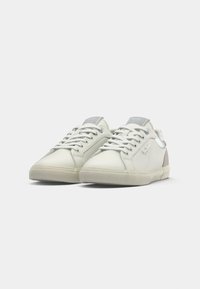 Sneakers bianchi con tomaia in sintetico liscio, dettagli grigi sulla linguetta e sul tallone, e lacci tono su tono. Suola in gomma testurizzata per una buona aderenza.