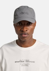 Szara czapka z lekko wygiętym daszkiem, teksturowanymi panelami i haftowanym logo „HALO 196819721981”. Biała koszulka z czarnym napisem i grafiką.