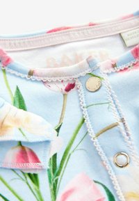 Un body floral azul claro con cierre a presión, delicados bordados en blanco y una etiqueta que dice "BAKER" de Ted Baker.
