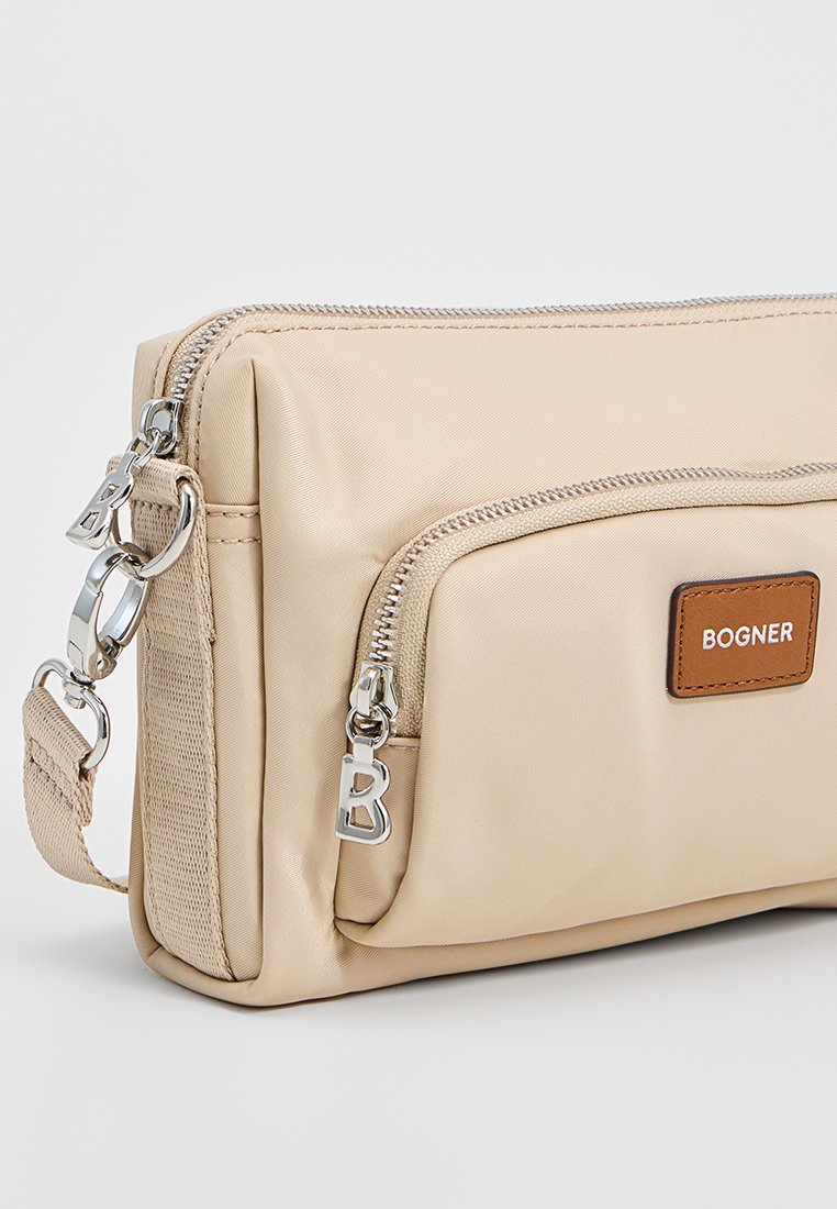 Beige Nylon Schultertasche mit silbernen Beschlägen, einer vorderen Reißverschlusstasche und einem braunen Leder-Logoschild. Mit abnehmbarem Schultergurt.