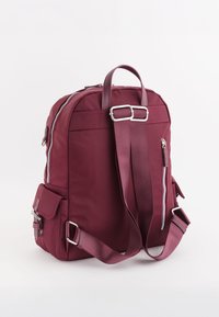 Mochila de nailon color malva con correas ajustables, cremalleras dobles, bolsillo lateral y un asa superior. Textura suave con sutiles detalles de costura.