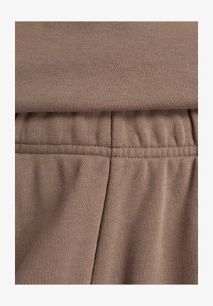 Ruskea poimuttuva kangas, jossa on joustava vyötärönauha ja rypytetty ommelvaikutelma vaatteessa.