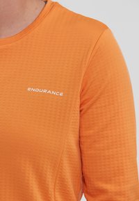 Langärmliges Sporthemd in leuchtendem Orange, mit einer strukturierten Stoffoberfläche und einem weißen "ENDURANCE"-Logo auf der Brust.
