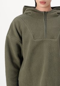 Olivinvihreä fleece-pullover, jossa on puoli-vetoketju, huppu ja teksturoitu kangas. Ominaisuuksiin kuuluvat istutetut hihat ja rento istuvuus.