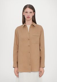 Brown button-up shirt with long sleeves, a chest pocket, and gold-tone buttons. The fabric has a subtle texture and a relaxed fit.