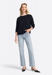 Maglione nero a maglia con texture a coste, abbinato a jeans diritto blu chiaro e scarpe nere con punta a punta. Design e vestibilità minimalisti.