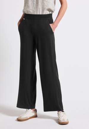Pantaloni neri a gamba larga realizzati in tessuto morbido, con vita elasticizzata e tasche laterali. Abbinati a sneakers bianche e beige.