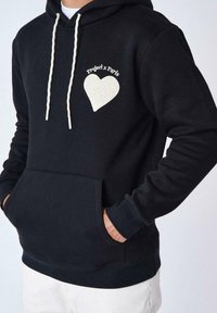 Sudadera de algodón negra con bolsillo frontal, cordones blancos y un logo de corazón texturizado etiquetado "Project x Paris" en el lado izquierdo del pecho.
