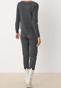 Pullover grigio a maglia con maniche lunghe e orlo a coste, abbinato a joggers grigi coordinati. Indossato con stivaletti bianchi alla caviglia.