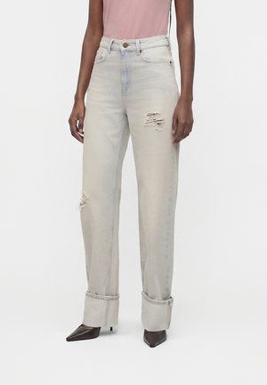 Hellgraue, distressed Jeans mit hoher Taille und breiten Umschlägen, kombiniert mit einem pinken Top und schwarzen spitz zulaufenden Pumps.