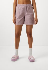 Lyserøde, teksturerede shorts med elastisk talje, kombineret med lyserøde slip-on sko og hvide ankelsokker. Enkel, afslappet pasform.
