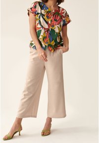 Haut à manches courtes à motifs floraux multicolores, associé à un pantalon large beige clair et des talons verts à brides.