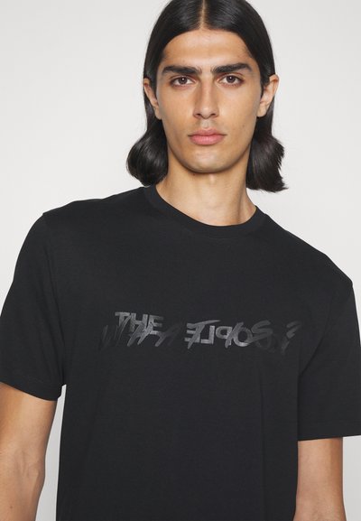 Black cotton T-shirt featuring a reflective text design across the chest. Short sleeves and a round neckline. Smooth texture.