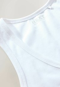White sleeveless cotton tank top with visible brand label printed inside the collar reading NEXT French Strap Vest.