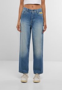 Plaša nagu zila denima džinsi ar izmītu mazgāšanu, ar priekšējām kabatām, pogu aizdari un zīmola uzlīmi netālu no jostasvietas.