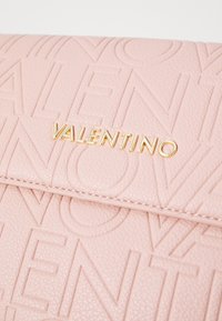 Vaaleanpunainen teksturoitu nahkalaukku, jossa on kohokuvioitu 'Valentino'-logo ja kultaiset metalliosat. Saumayksityiskohdat lisäävät eleganssia muotoiluun.