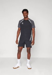 Herridrottsoutfit i svart, med en kortärmad tröja med grå accenter och vita randdetaljer, i kombination med matchande shorts och vita skor.