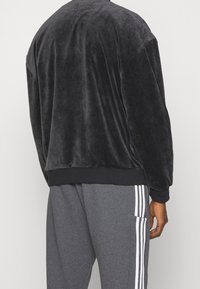 Svart velourtröja med avslappnad passform, som har ribbade muddar och midja. Matchad med grå byxor med vita vertikala ränder.